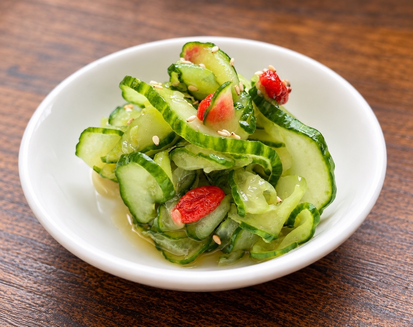 Thinly sliced cucumber with red goji berries and white sesame seeds in a white bowl