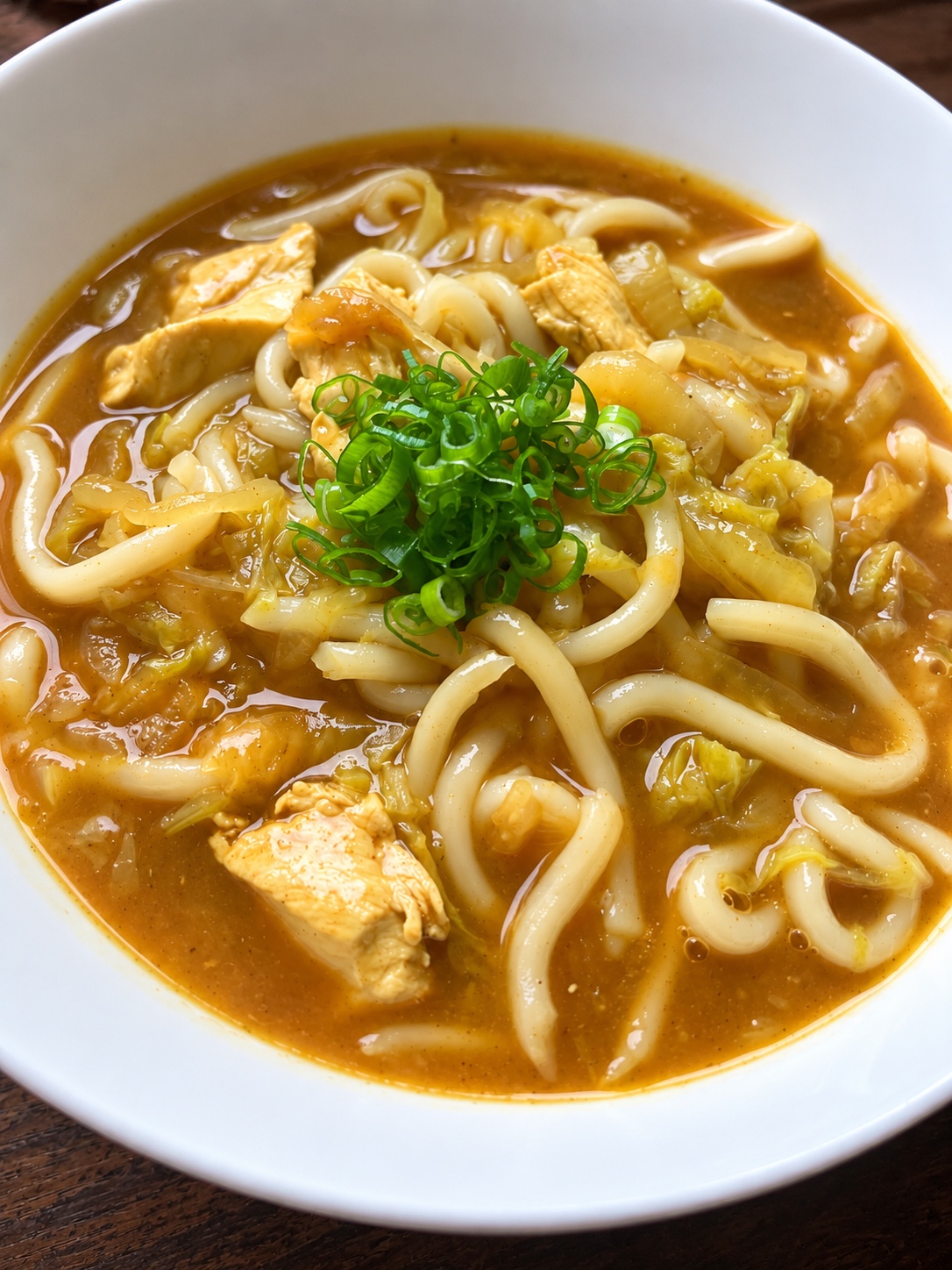 Curry udon with chicken and vegetables in a white bowl, topped with green onions