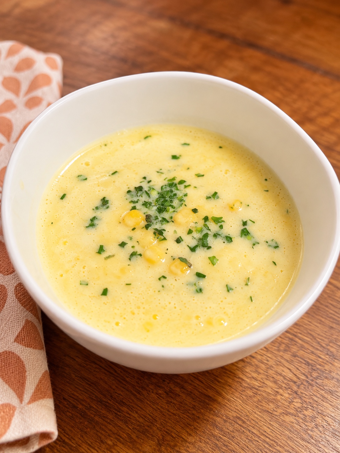 Smooth yellow corn potage in a white bowl, topped with corn and parsley