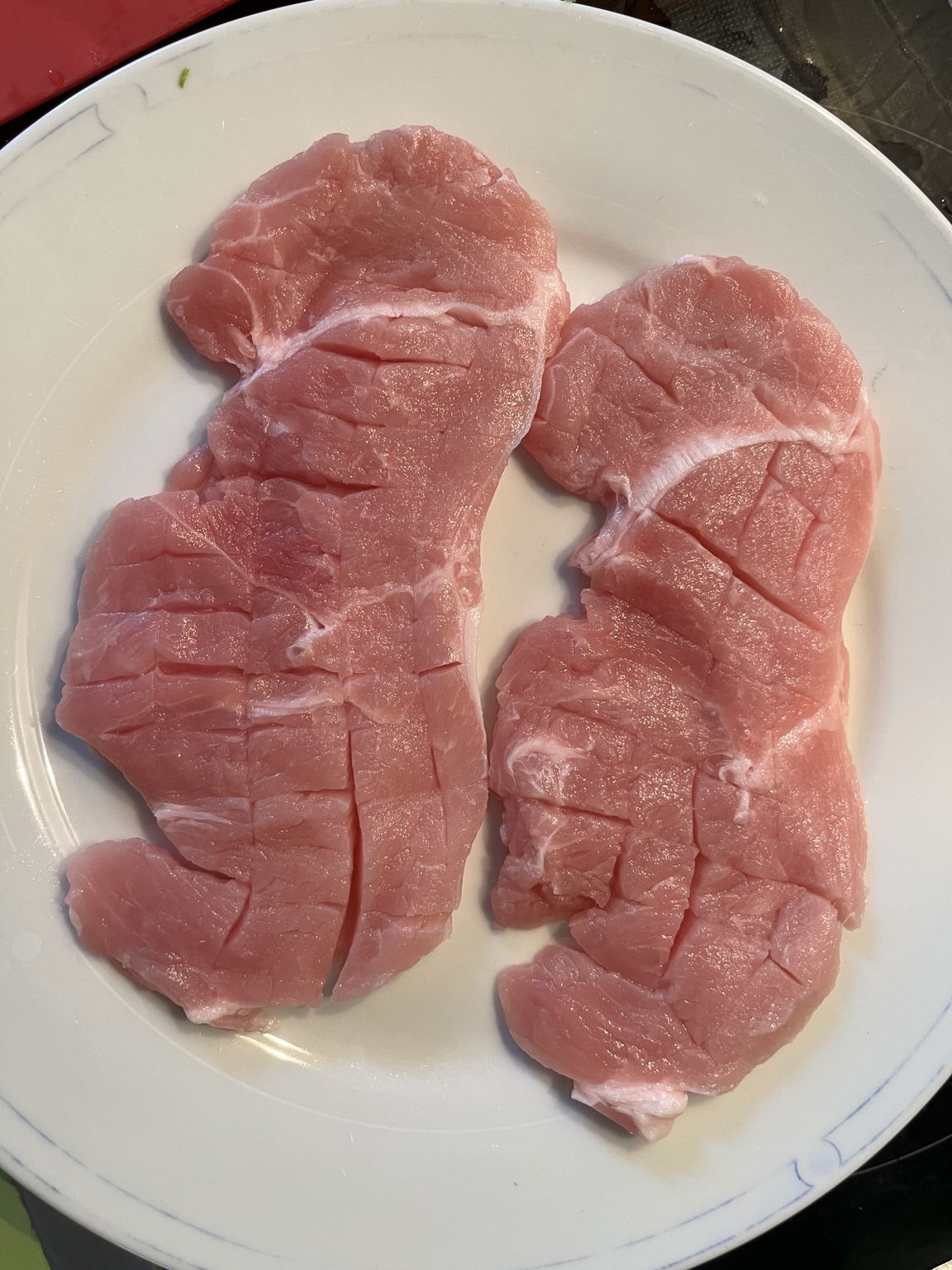 Two raw pork minute steaks with shallow cuts scored across the surface