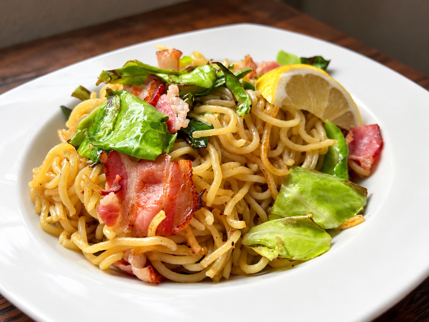 Lemon salt yakisoba with bacon, cabbage and a lemon wedge on a white plate