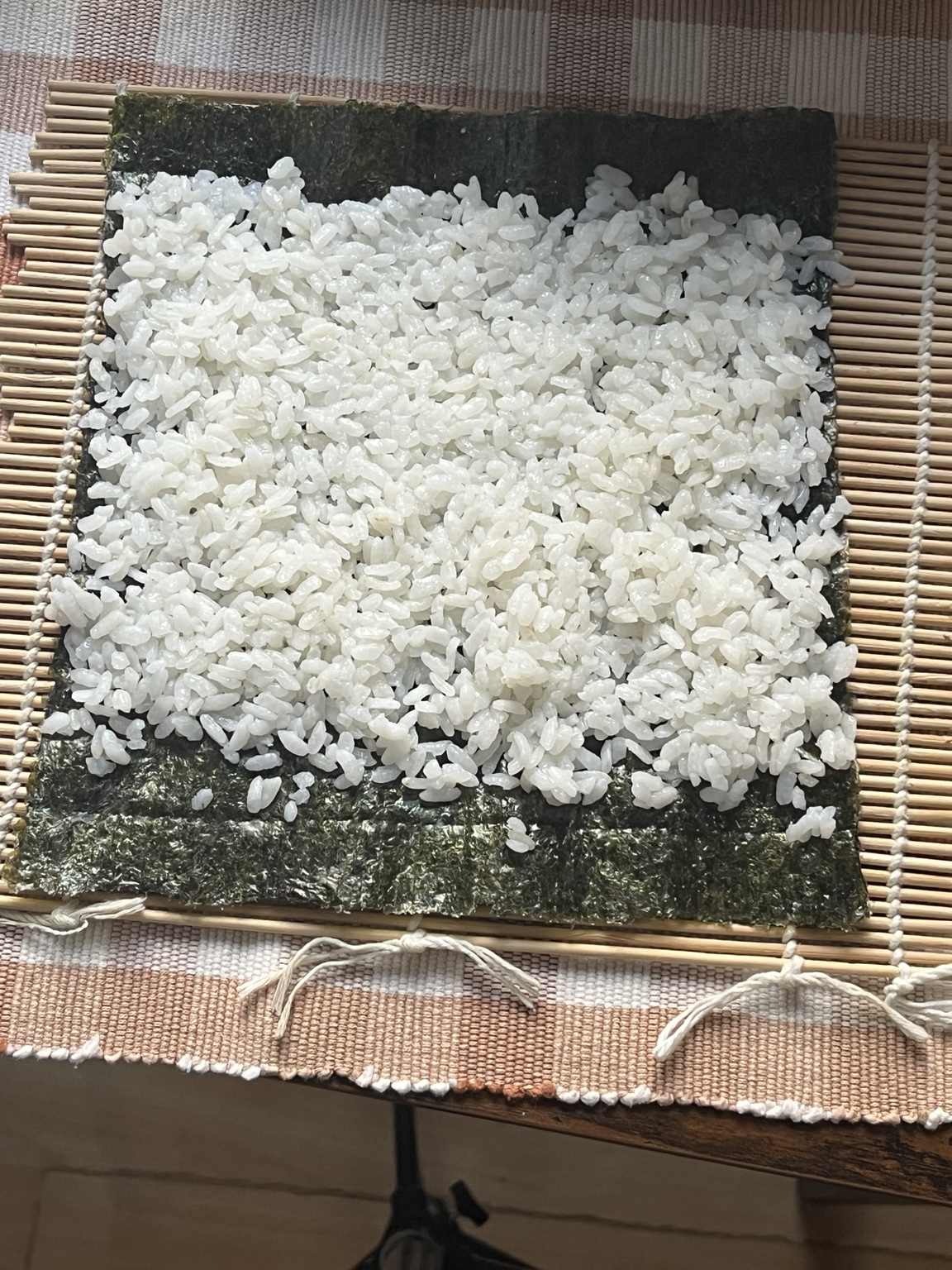 Sushi-Reis wird auf einem Nori-Blatt verteilt, wobei oben und unten ein Rand frei bleibt