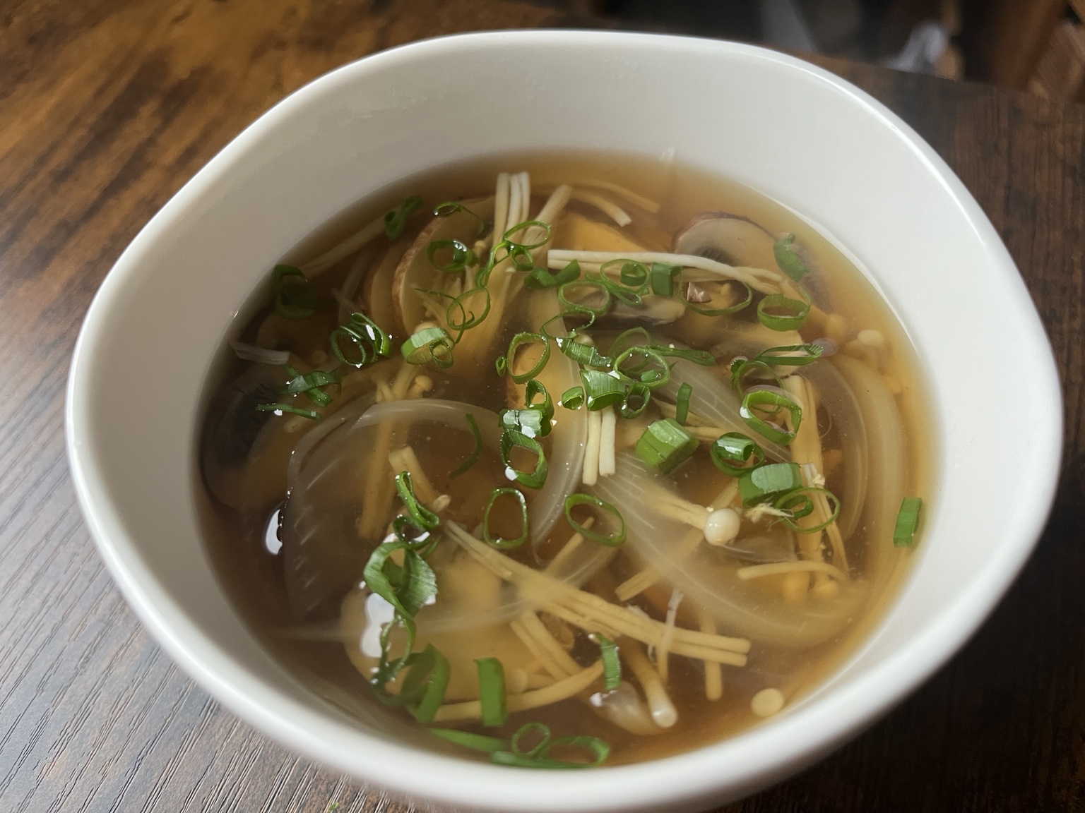 Clear mushroom and onion soup with spring onions in a white bowl