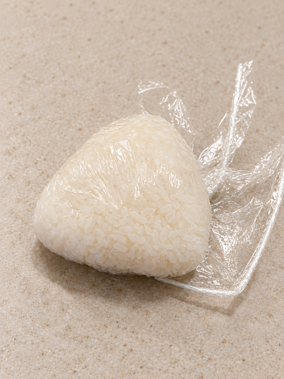 Ein dreieckiges Onigiri wird in Frischhaltefolie geformt