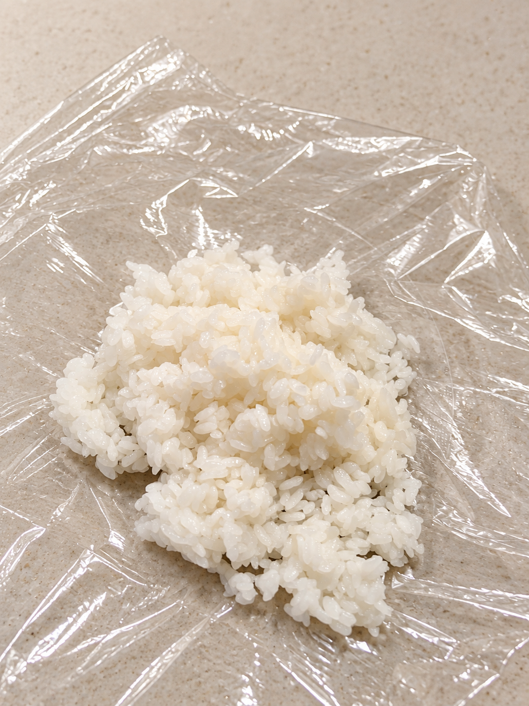 Eine Portion gekochter Reis auf Frischhaltefolie zum Formen eines Onigiri