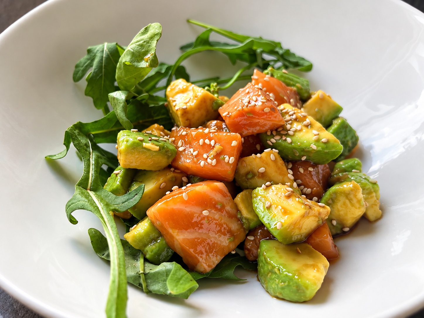 Frischer Lachs-Avocado-Salat mit Sesam auf Rucola, serviert in einer weißen Schüssel.