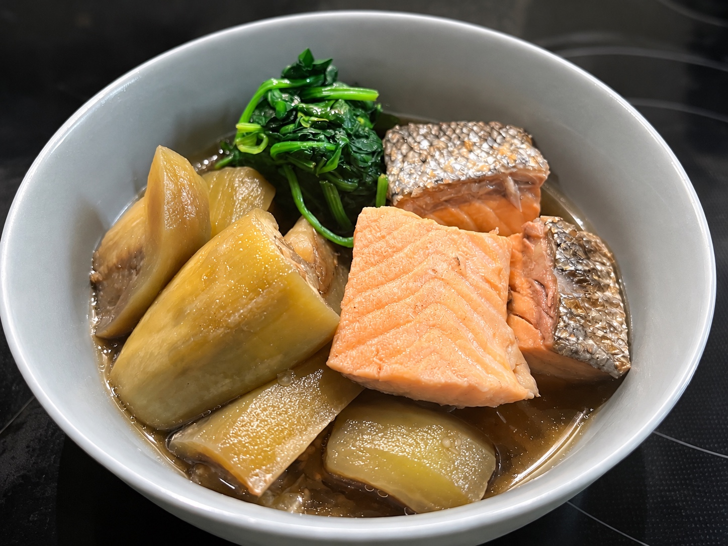 Salmon and peeled eggplant in dashi broth with spinach in a white bowl