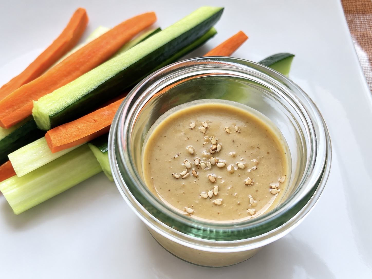 Sesame miso dressing in a glass bowl with carrot and cucumber sticks