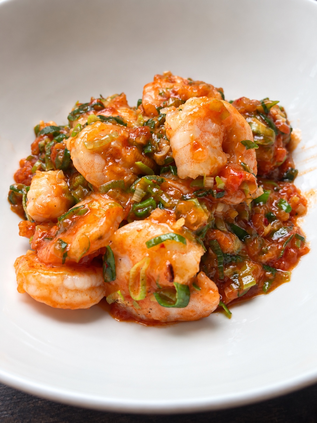 Shrimp in glossy chili sauce with chopped spring onions on a white plate